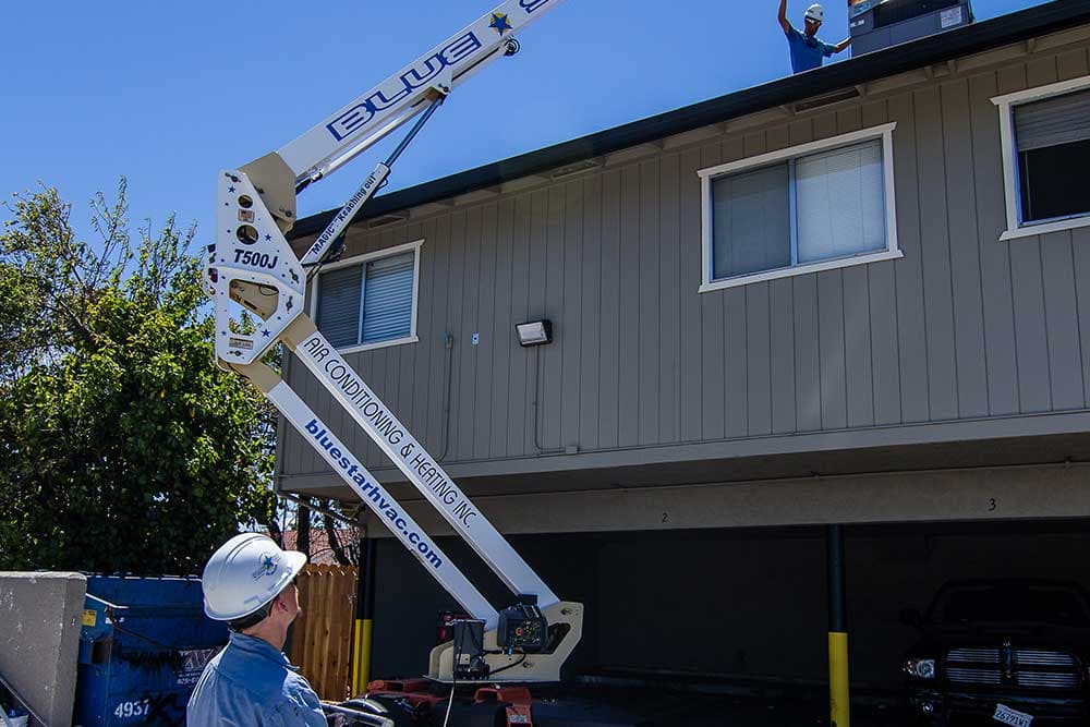 Magic, Blue Star's JLG T500J towable lift, raising equipment to a technician on a two-story apartment roof
