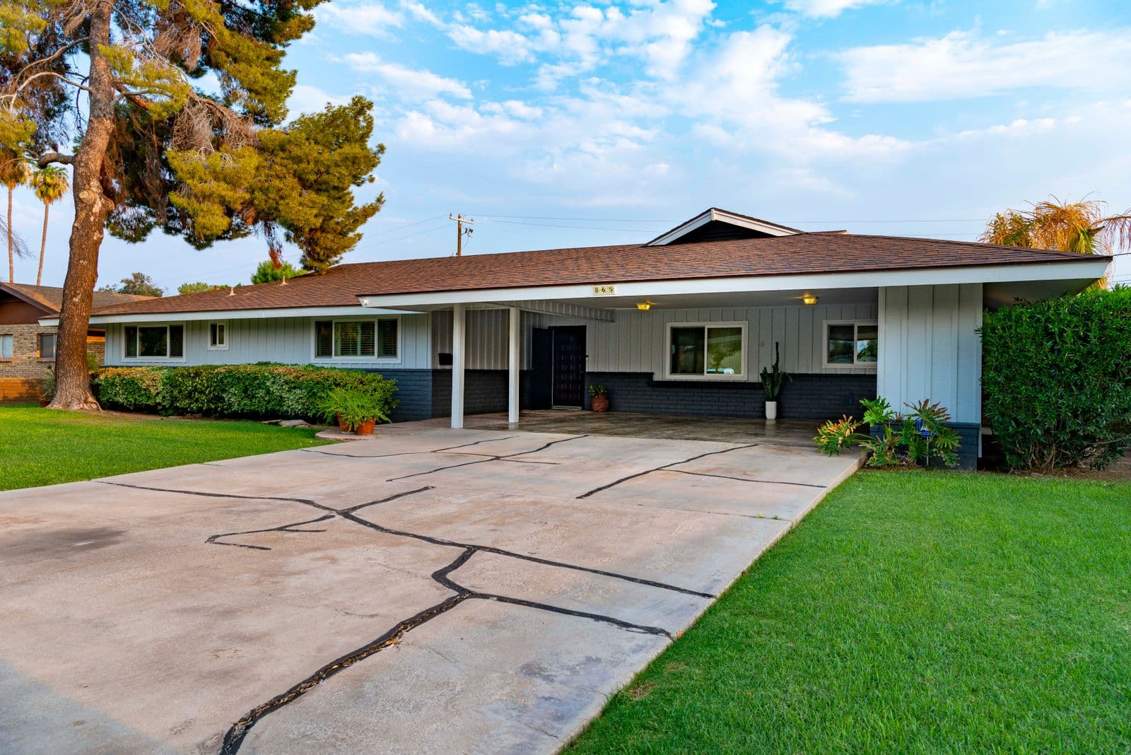Low-slung 1950s-style ranch house with a carport, wide driveway and green lawn