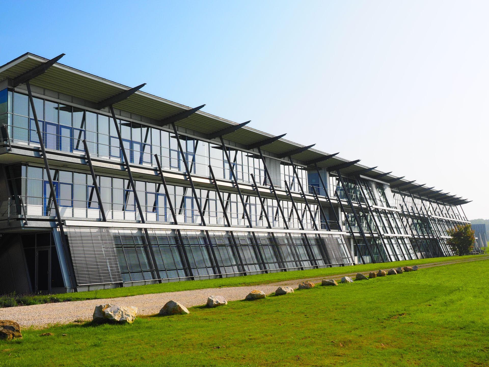 Long low-rise commercial building with a glazed facade and sunshades above a green lawn