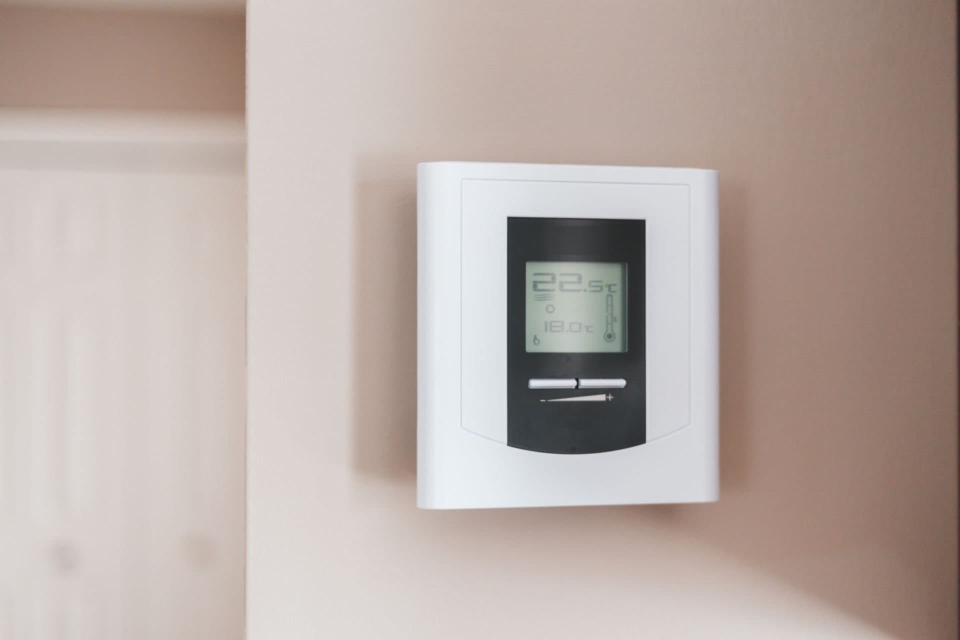 White digital programmable thermostat mounted on a warm beige interior wall