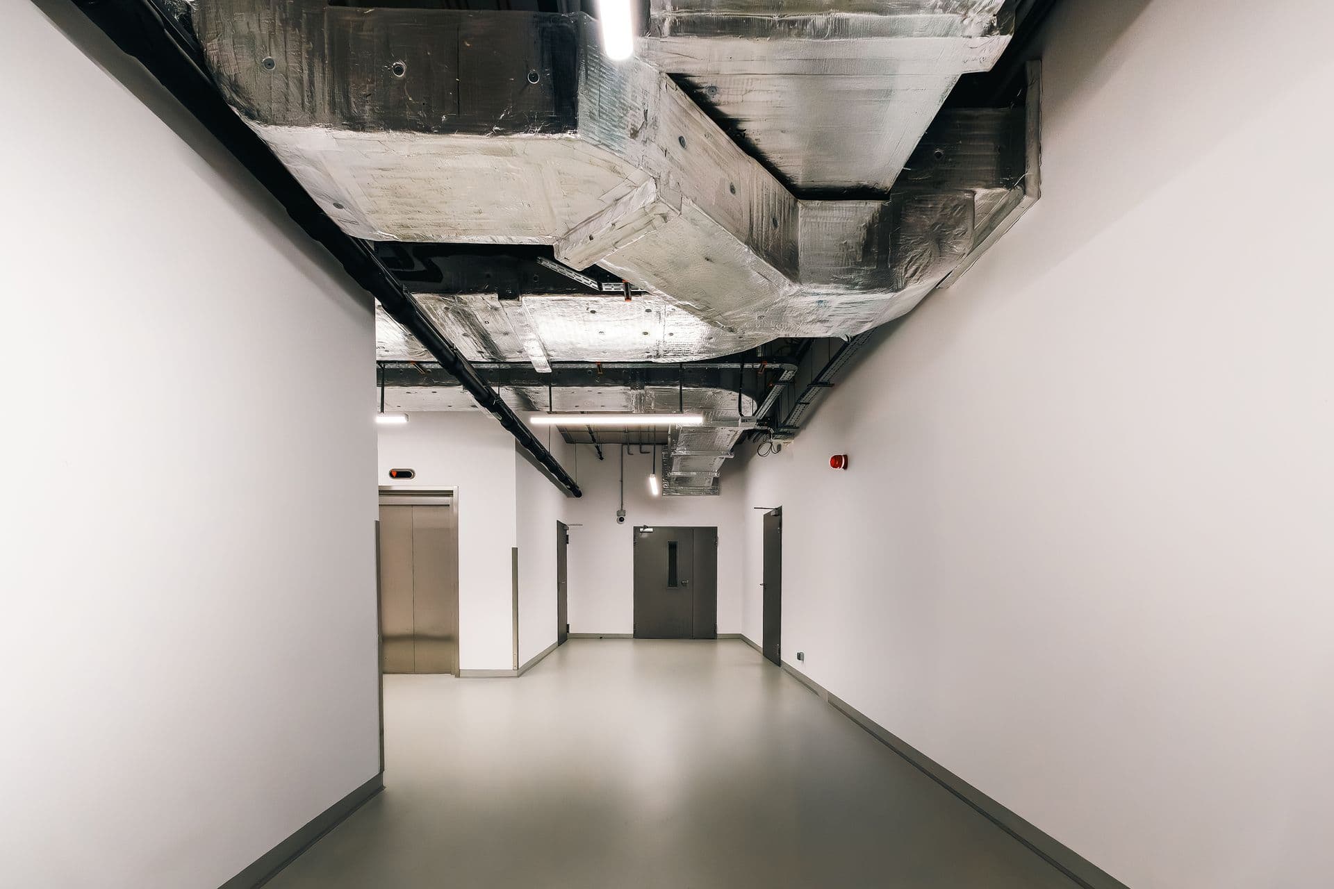 Exposed galvanized HVAC ductwork running along the ceiling of a bright commercial corridor