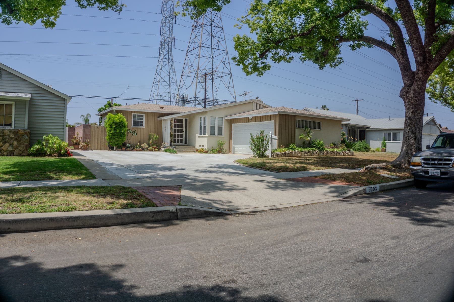 Street of single-story mid-century tract homes with driveways and lawns under power-line towers