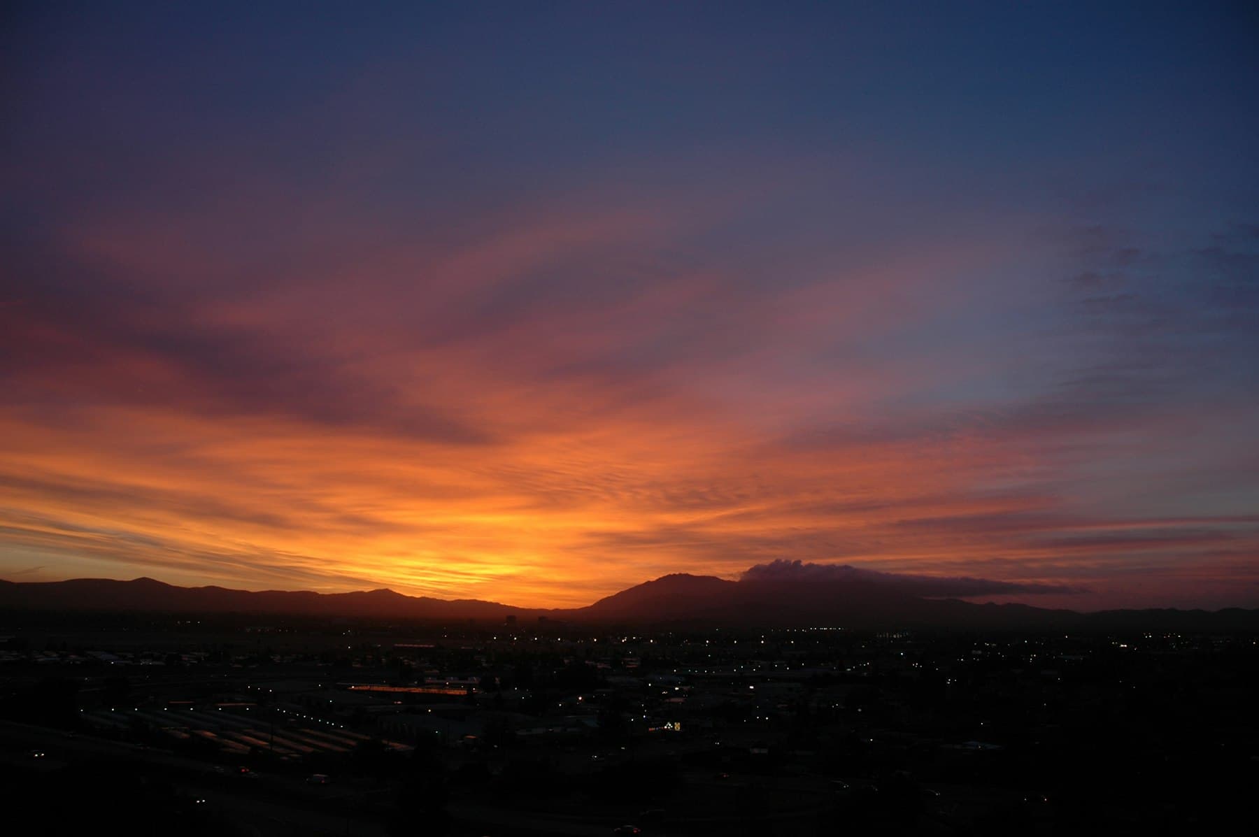 Orange sunset sky over the silhouette of Mount Diablo, with the lights of Concord below