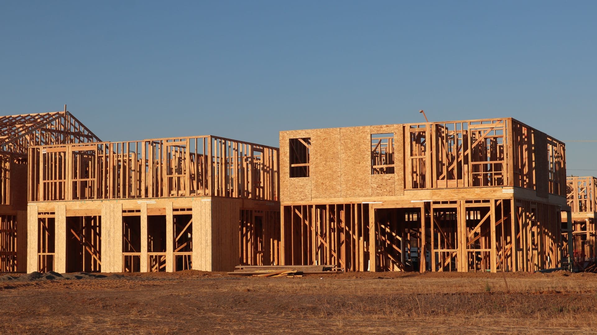 Wood-framed two-story homes under construction in a California subdivision on a clear day