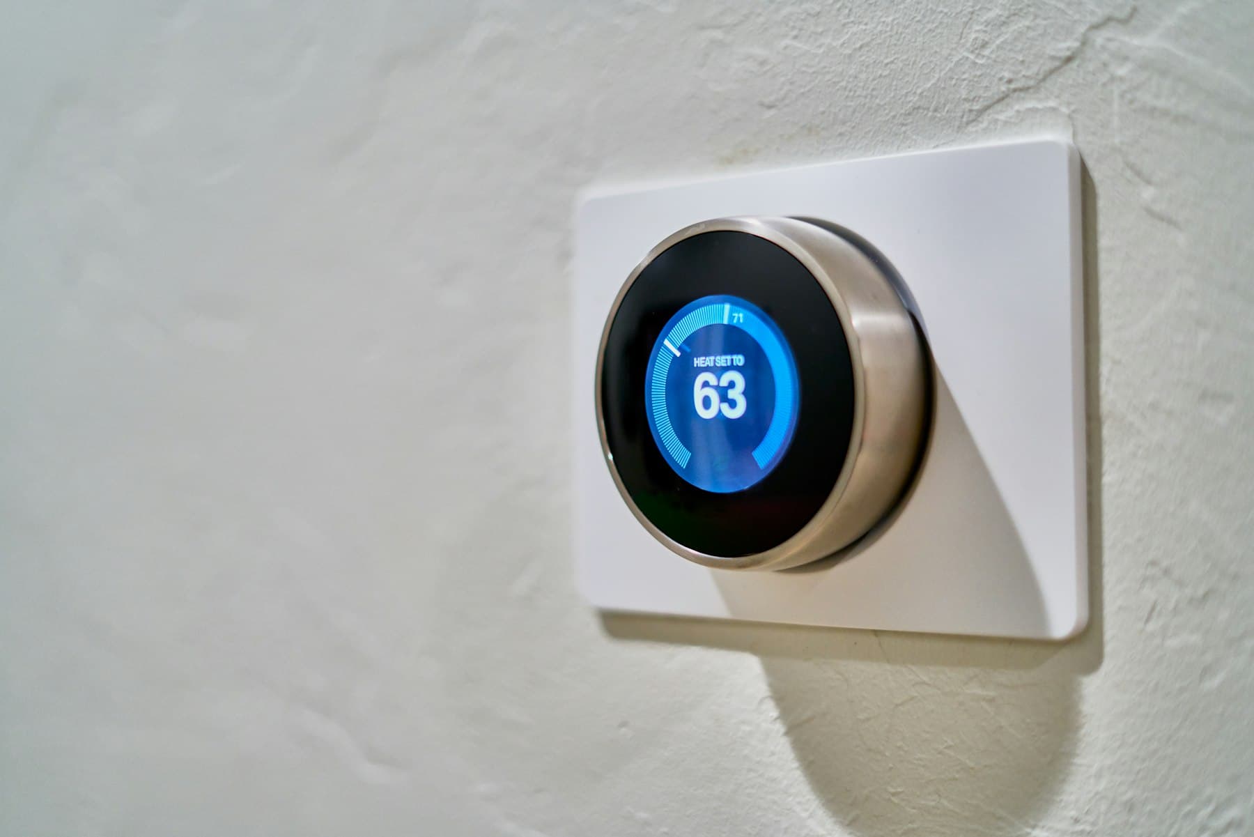 Nest smart thermostat showing 63 degrees on a white textured wall