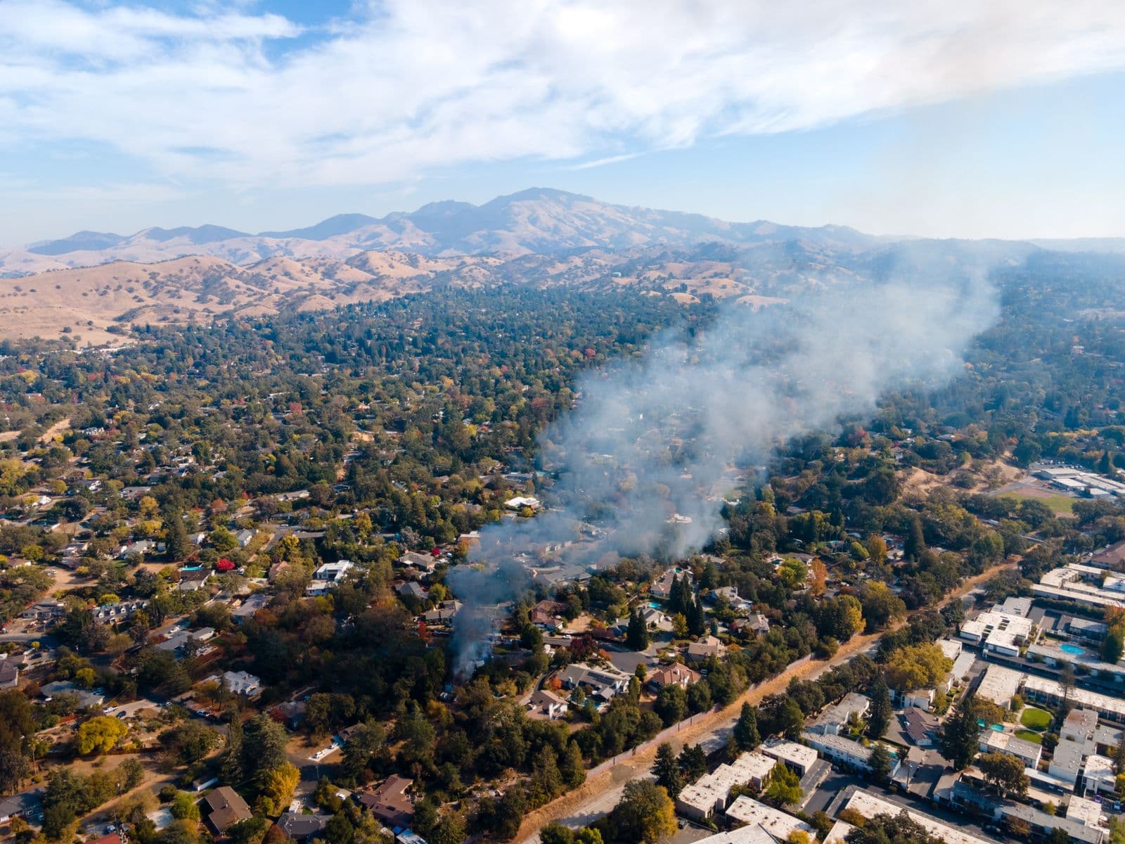 Aerial view of a smoke plume drifting over a Walnut Creek neighborhood, with Mount Diablo beyond