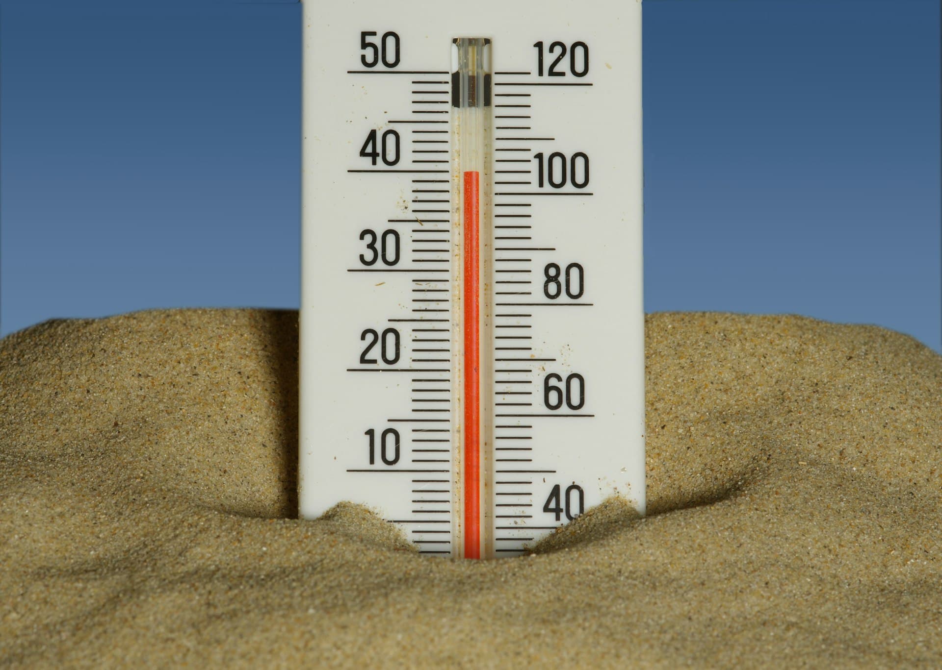 Thermometer in sand reading close to 40°C (about 100°F) against a clear blue sky