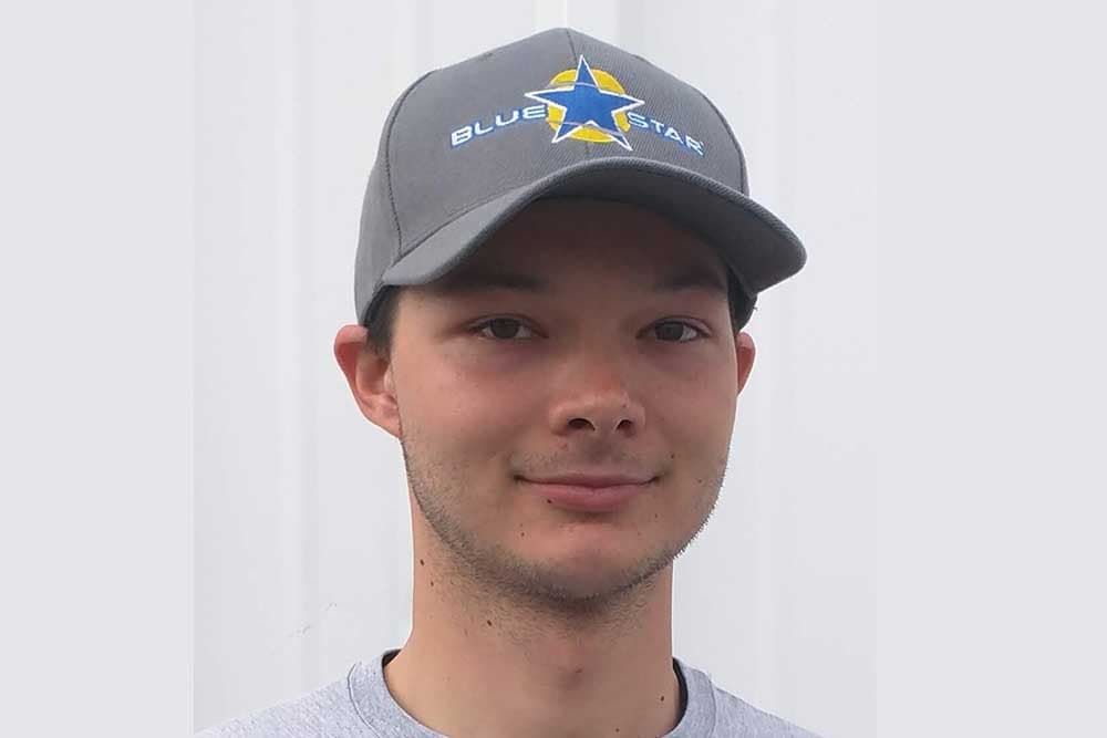 Colten of Blue Star in a grey Blue Star cap against a white wall