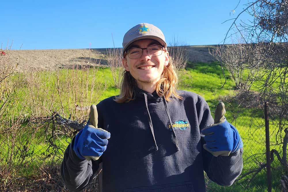 Gabe of Blue Star giving two gloved thumbs up on a green hillside under a blue sky