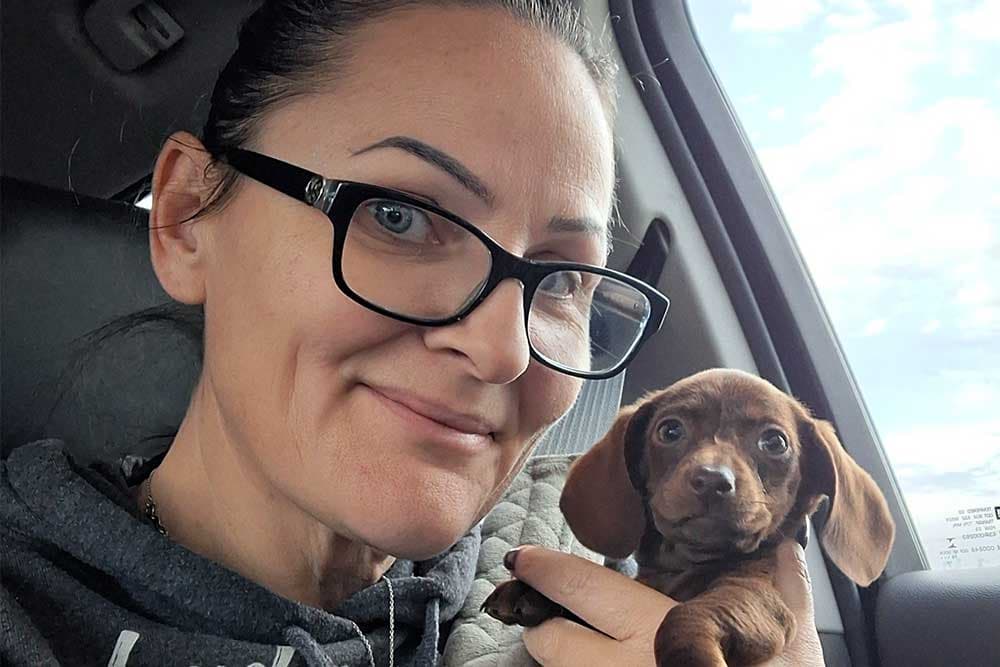 Pilar of Blue Star in black glasses, holding Georgi, the team's chocolate mini-Dachshund puppy
