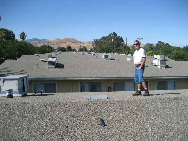 Blue Star team member on an apartment complex roof dotted with dozens of HVAC units, with golden hills beyond