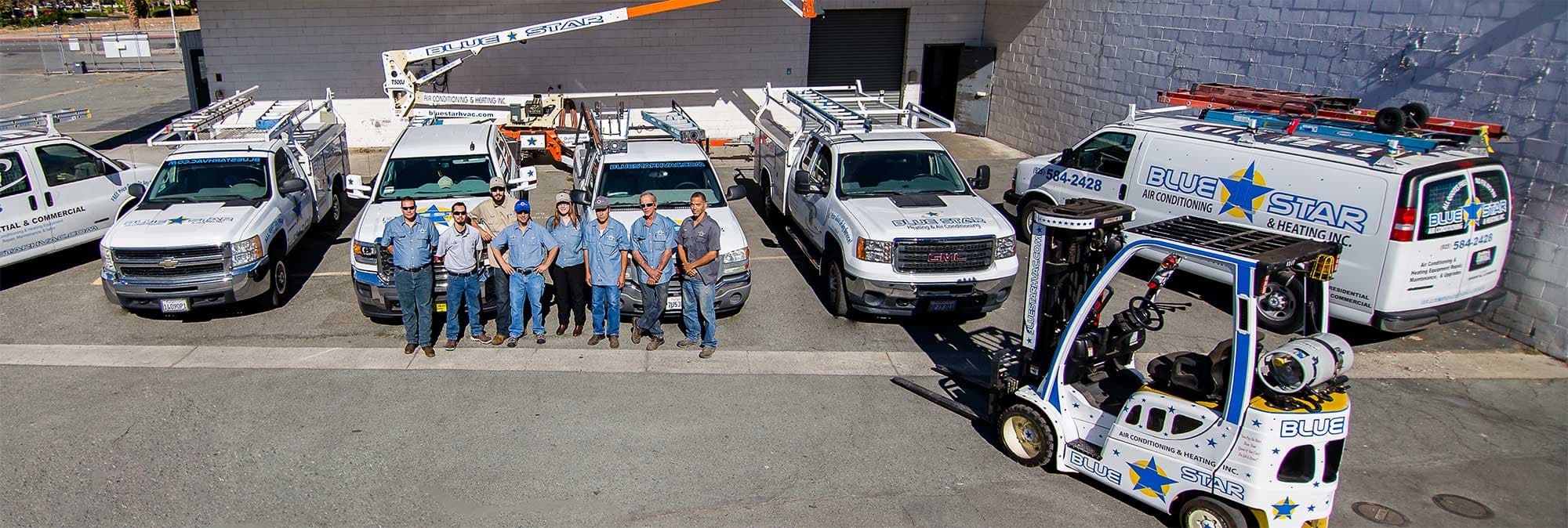 Blue Star crew lined up in the company yard in front of their white service trucks, a van and the star-decorated forklift
