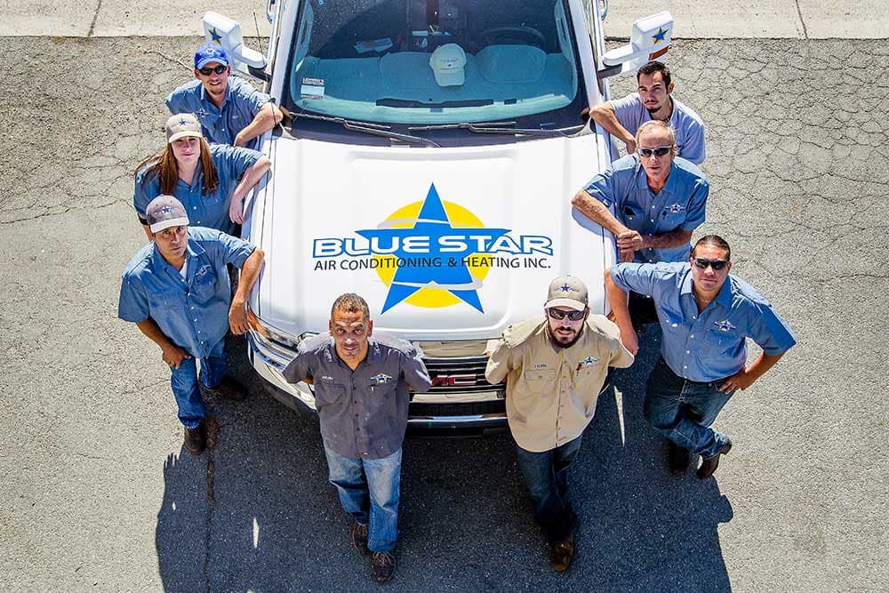 Overhead view of nine Blue Star team members in work shirts gathered around the hood of a white truck bearing the Blue Star logo