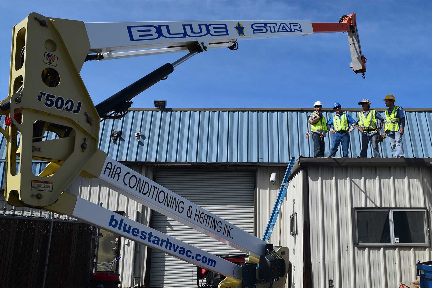 Blue Star crew in safety vests on a metal commercial roof beside the company's lift boom marked bluestarhvac.com