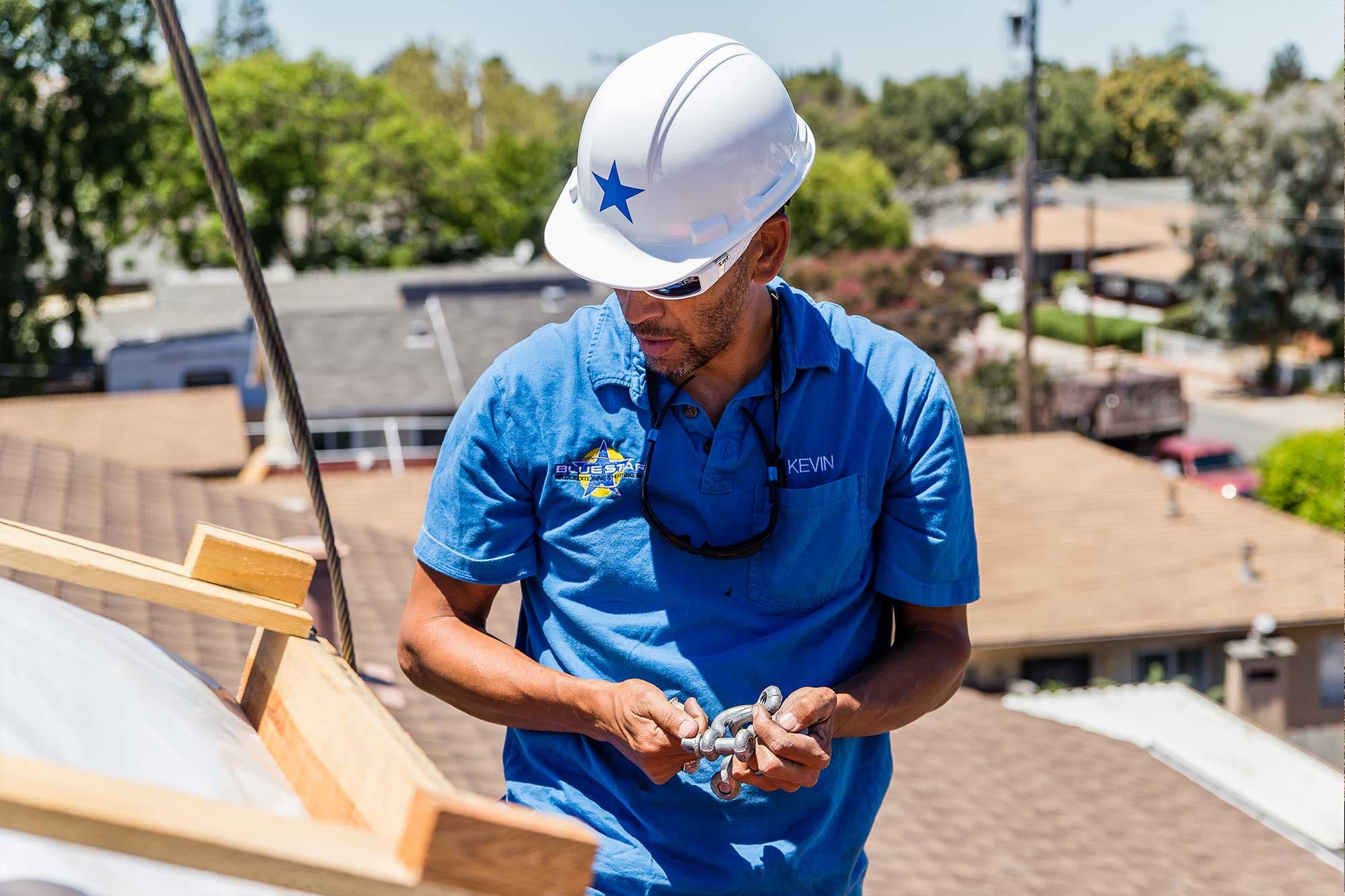 Kevin of Blue Star in a white hard hat working on a residential roof above neighboring houses