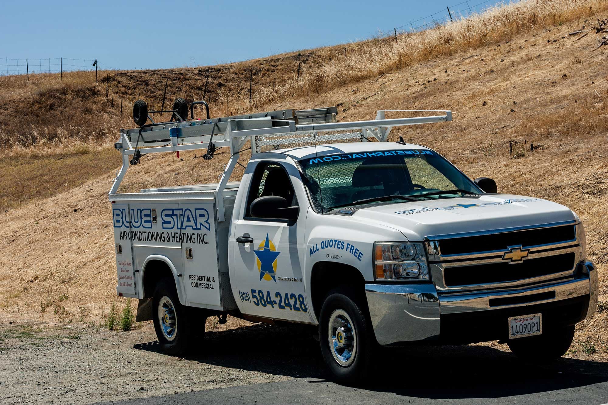 Zena, a white Blue Star utility truck with a ladder rack, parked below a dry golden hillside