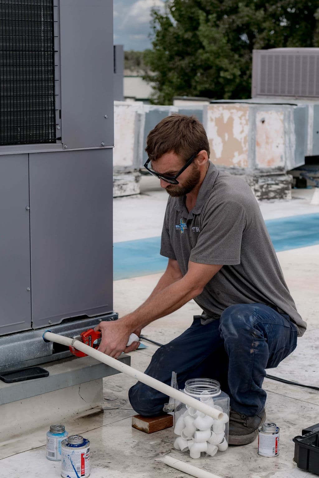 Blue Star technician cutting white PVC pipe beside a rooftop HVAC unit