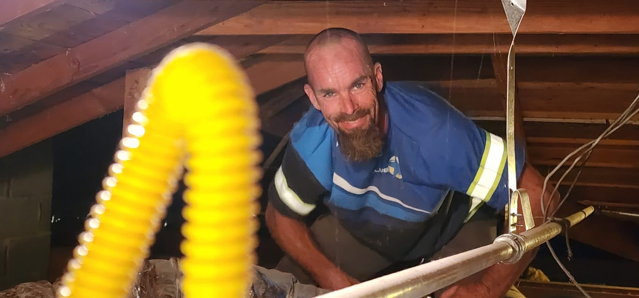 Smiling Blue Star technician crouched in an attic beside yellow-coated flexible gas piping